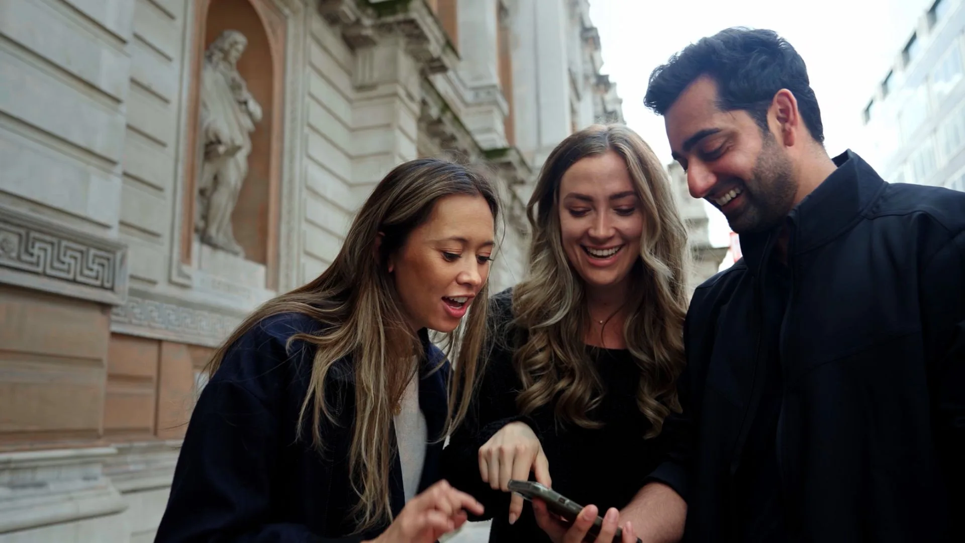 A group of friends reading a riddle on a phone on a quiet London side street during a treasure hunt